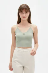 Musculosa de tejido rib color verde menta, con tirantes finos, escote en V adornado con detalles de encaje y un pequeño lazo decorativo en el centro.