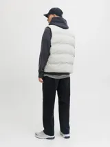 Chaleco puffer acolchado de color gris claro, con cuello alto y cierre frontal con cremallera. Cuenta con bolsillos laterales y diseño versátil sin mangas.