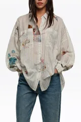 Camisa oversize de manga larga con patrón de rayas y estampado artístico multicolor, con cuello camisero, cierre frontal de botones y bolsillos en el pecho.