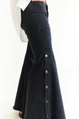 Jean de corte oxford con tiro medio, confeccionado en denim negro. Presenta recortes curvos en las piernas y detalle de botones metálicos en los laterales de la botamanga.