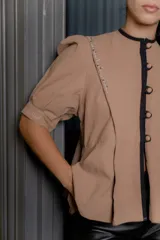 Chaqueta gris de silueta femenina con mangas abullonadas, cuello redondo y cierre frontal con botones forrados. Presenta detalles de bordado artesanal a mano en los hombros y solapas.