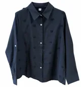 Camisa negra de manga larga con cuello camisero, cierre frontal de botones y detalles de pequeños pompones distribuidos por toda la prenda.