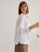 Camisa de corte recto y manga larga, confeccionada en algodón blanco. Presenta un canesú superior con bordado inglés floral y detalle de placa metálica con logo en la espalda.
