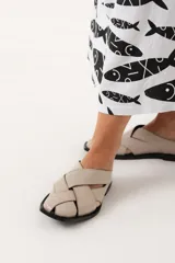 Zuecos color hueso con diseño de tiras cruzadas y suela plana color negro.