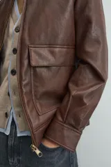 Sobrecamisa de corte relajado confeccionada en tejido efecto piel color marrón. Presenta cuello solapa, cierre frontal con cremallera, mangas largas con puños abotonados y dos bolsillos de plastrón con solapa en la parte frontal.