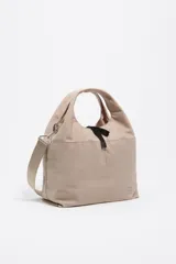 Bolso bandolera de estructura blanda marca Bimba y Lola, confeccionado en nylon con detalles en cuero. Presenta doble asa de mano, correa de tejido regulable y extraíble, cierre de cordón ajustable y logo metálico en el frente.
