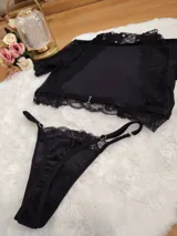 Conjunto de lencería compuesto por un top de cuello alto y una tanga, confeccionados en terciopelo negro con detalles de encaje y microtul. El top presenta mangas cortas con terminaciones en encaje y el borde inferior decorado con una cinta y encaje. La tanga es regulable y combina la textura del terciopelo con bordes de encaje.