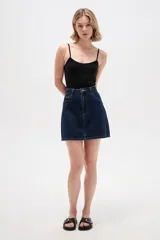 Minifalda de denim en color azul oscuro, con tiro alto, bolsillos delanteros y traseros, costuras en contraste y cierre frontal con botón y cremallera.