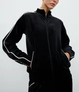 Campera deportiva de plush color negro con cuello alto, cierre frontal por cremallera, bolsillos laterales y detalle de piping blanco contrastante en mangas y bolsillos.