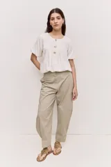 Blusa blanca de manga corta, con escote redondo y cierre frontal con tres botones. Presenta pliegues frontales y diseño liviano.