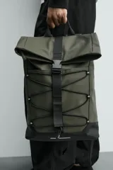 Mochila técnica de acabado engomado en color negro. Presenta un diseño de solapa con cierre de hebilla de liberación rápida y un sistema de cordones elásticos frontales. Incluye compartimento para dispositivos electrónicos, espalda acolchada y correas ajustables.