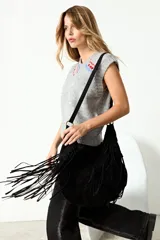 Cartera bandolera de gamuza sintética color negro, con diseño de flecos largos en los laterales y correa ajustable.