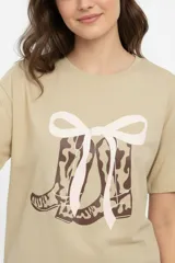 Remera de algodón color beige con estampado frontal de un corazón rosado que contiene un moño. Tiene cuello redondo y mangas cortas.