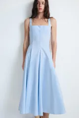 Vestido midi de color celeste con escote cuadrado y tirantes anchos. Presenta un diseño entallado en el torso con falda acampanada terminada en godets que aportan volumen y movimiento. Incluye cierre lateral con cremallera oculta.