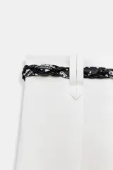Pantalón de popelina de tiro alto y pernera ancha, de color negro. Presenta pinzas delanteras, bolsillos laterales y falsos bolsillos de vivo en la espalda. Incluye un cinturón combinado tipo pañuelo trenzado con tiras colgantes y cuentas de madera. Cierre frontal con cremallera, botón interior y gancho.