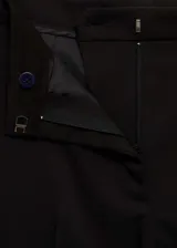 Pantalón de traje negro de tiro medio, con diseño recto y trabillas para cinturón. Cuenta con bolsillos laterales y dos bolsillos de ribete en la parte posterior, además de dobladillo vuelto en los tobillos.
