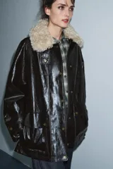 Chaqueta de efecto cuero color marrón oscuro con acabado brillante, cuello de solapa con aplicación de pelo sintético extraíble, manga larga con trabillas, bolsillos frontales de plastrón con solapa y cierre frontal con cremallera y botones a presión.
