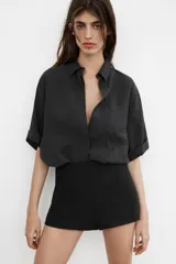 Camisa de corte fluido confeccionada en mezcla de modal, con cuello solapa, manga corta con dobladillo y bolsillo de plastrón en el delantero. Presenta cierre frontal con botones ocultos por tapeta y aberturas laterales en el bajo.