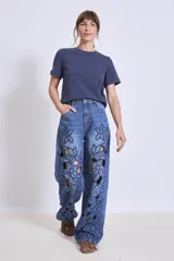 Pantalón de jean azul con bordados florales y aberturas en forma de flor en las piernas.