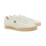 Championes Lacoste modelo Aura, color blanco con suela de goma en tono beige. Presentan un diseño minimalista de cuero con el logo del cocodrilo metálico en el lateral y detalles perforados.