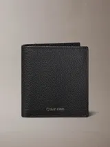 Billetera plegada Calvin Klein de cuero con textura granulada. Cuenta con compartimento para billetes, cinco ranuras para tarjetas y una solapa transparente para identificación. Presenta el logo de la marca grabado en lámina metálica en el frente.