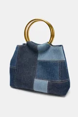 Bolso de hombro tipo mini saca con cuerpo en patchwork de denim en tonos azules. Posee una anilla metálica dorada como asa de mano y una correa bandolera extraíble.