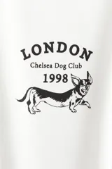 Remera blanca de manga corta con cuello redondo y corte holgado. Presenta un pequeño estampado en el pecho con el texto "LONDON Chelsea Dog Club 1998" y la silueta de un perro salchicha.