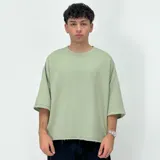 Remera verde clara de corte boxy, con mangas 3/4 y cuello redondo. Tiene un bordado con el número 1999 en el pecho y el ruedo desflecado.