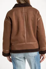 Chaqueta tipo gamulán de calce oversize en color marrón, con cuello y ribetes de corderito en contraste. Presenta cierre frontal de cremallera, bolsillos laterales y detalles de tiras decorativas en material sintético.