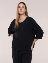 Blusa oversize color negro con caída fluida, escote redondo, bolsillo frontal en el pecho, mangas tres cuartos de hombro caído y costuras a la vista en contraste.