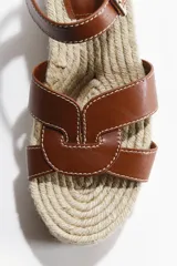 Sandalias de tacón corrido con plataforma de yute trenzado, tiras de cuero marrón en el empeine y tira ajustable con hebilla en el tobillo.