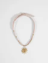 Collar con dije de sol en tono dorado y cordón de tela con estampado de cuadros vichy en tonos rosados. Presenta pequeñas cuentas metálicas doradas distribuidas a lo largo del cordón.