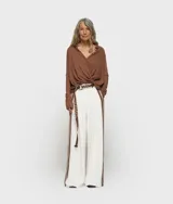 Blusa cruzada de punto de algodón orgánico color marrón, con cuello, cierre de botón, puños con abertura y monograma bordado en la manga izquierda. Tiene bajo recto y aberturas laterales.