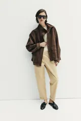 Chaqueta de tejido efecto ante color marrón, con cuello alto, cierre frontal con cremallera y botones a presión, manga larga y bolsillos de plastrón con solapa en el delantero.