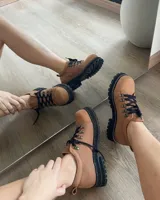 Zapatos tipo borceguíes bajos de cuero vacuno color tostado, con suela track negra de goma y cordones negros con ganchos metálicos.