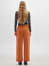 Pantalón ancho y suelto de tejido tipo terciopelo color naranja, con cintura elástica y cordón ajustable. Presenta detalles de pespuntes decorativos a los lados.