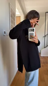 Sweater de punto negro oversize, con cuello redondo y hombros caídos, de manga larga y silueta amplia. Presenta bordado artesanal en el frente con la frase "e pur si muove" y líneas en contraste en los hombros.