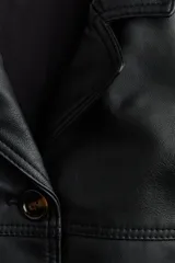 Campera negra de cuero sintético con solapas de muesca, cierre frontal de botones oscuros y bolsillos laterales ribeteados. Presenta costuras de canesú en el frente y en la espalda, y diseño forrado.