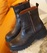 Botas de cuero marrón con suela track de goma negra, cierre lateral en color rojo y detalle de tira trasera al tono.