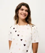 Blusa de pijama de manga corta con cuello redondo y corte regular, confeccionada en tejido peach touch con estampado de corazones pequeños en tonos neutros.