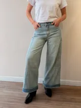 Pantalón jeans tipo palazzo de corte amplio y tiro medio-alto, con lavado celeste vintage y dobladillo vuelto con detalle de rayas en la terminación. Cuenta con bolsillos delanteros y traseros.