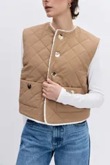 Chaleco reversible de diseño acolchado con costuras en rombos, color tostado con interior de corderito blanco. Presenta cierre frontal con botones, cuello redondo y bolsillos delanteros.