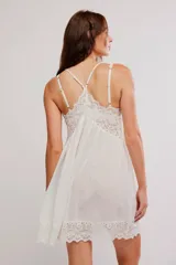 Vestido corto tipo slip dress color blanco, de corte amplio tipo babydoll, confeccionado en mezcla de viscosa y algodón. Presenta escote en V con apliques de encaje, tiras finas regulables y ruedo festoneado con detalles de encaje y calados.