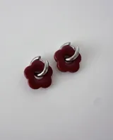 Aros de acero quirúrgico con argolla plateada y dije de flor translúcida en color lila con lunares negros.