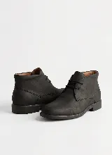 Bota corta tipo botineta de cuero negro con textura granulada, cierre mediante cordones y suela plana de goma.