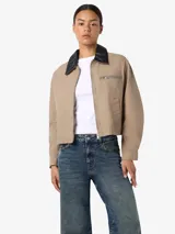 Chaqueta estilo worker de gabardina en color beige, con cuello camisero de cuerina negra, cierre frontal de cremallera y bolsillos frontales con cierre y ribete.