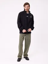 Campera Rusty de corte clásico, color negro, con cierre frontal completo, cuello alto y puños elásticos. Presenta un diseño minimalista con el logo de la marca bordado en el pecho.