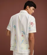 Camisa de lino y algodón color blanco con cuello inglés, manga corta y cierre frontal de botones. Presenta un diseño de bordado fino floral y de aves de estilo artesanal.