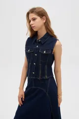 Chaleco de denim azul oscuro con bolsillos con solapa en el pecho, cierres decorativos y cierre frontal con botones metálicos.