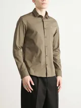 Camisa de vestir color marrón, corte slim, de popelín de algodón elástico, con cuello clásico, cierre frontal con botones y logo "ck" bordado en el pecho.